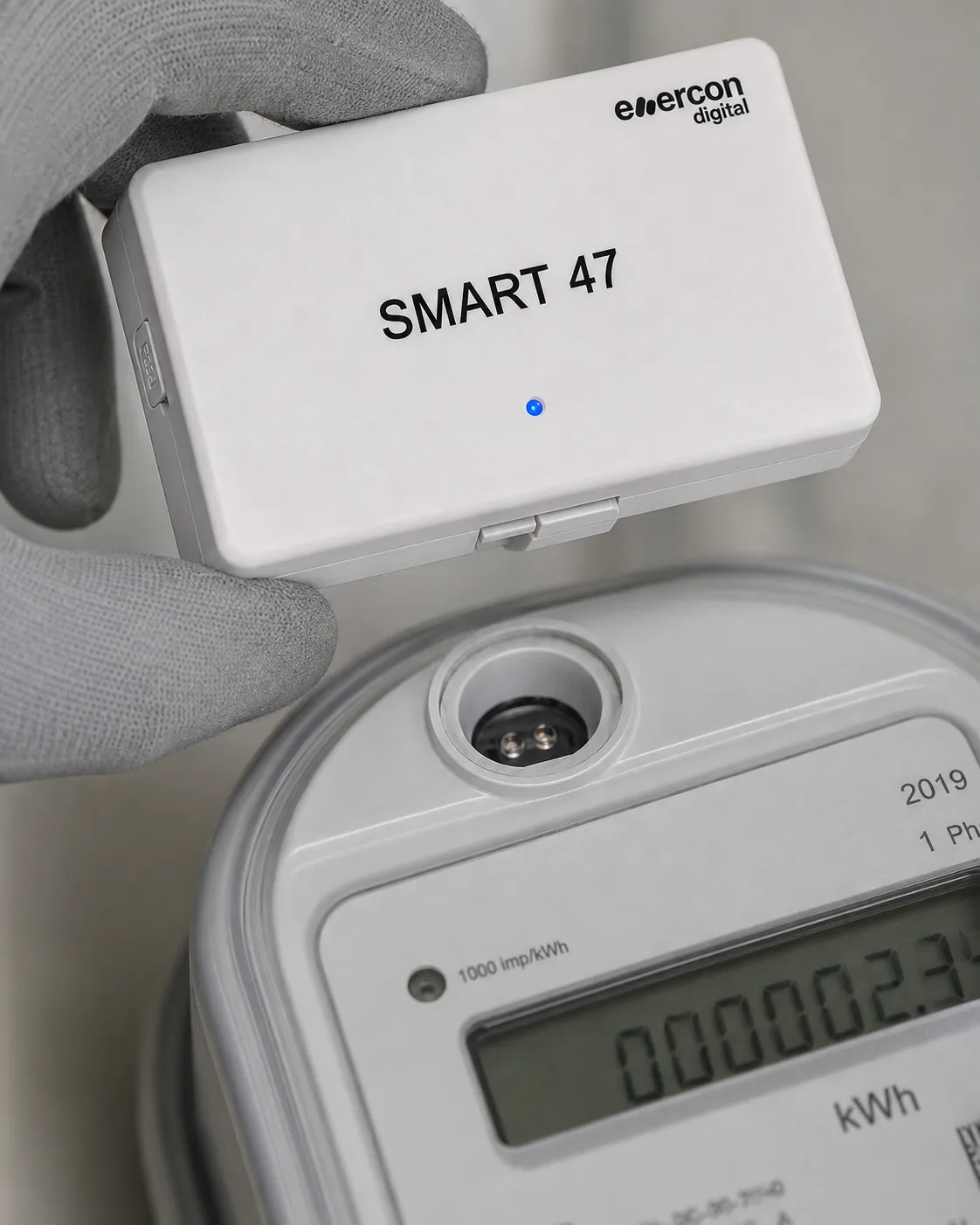 A gloved hand holding the Smart47 unit against the face of a single-phase meter, aligning it with the optical port